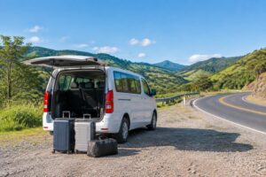 Van de nove lugares branca estacionada em um mirante de estrada com malas ao lado e morros ao fundo